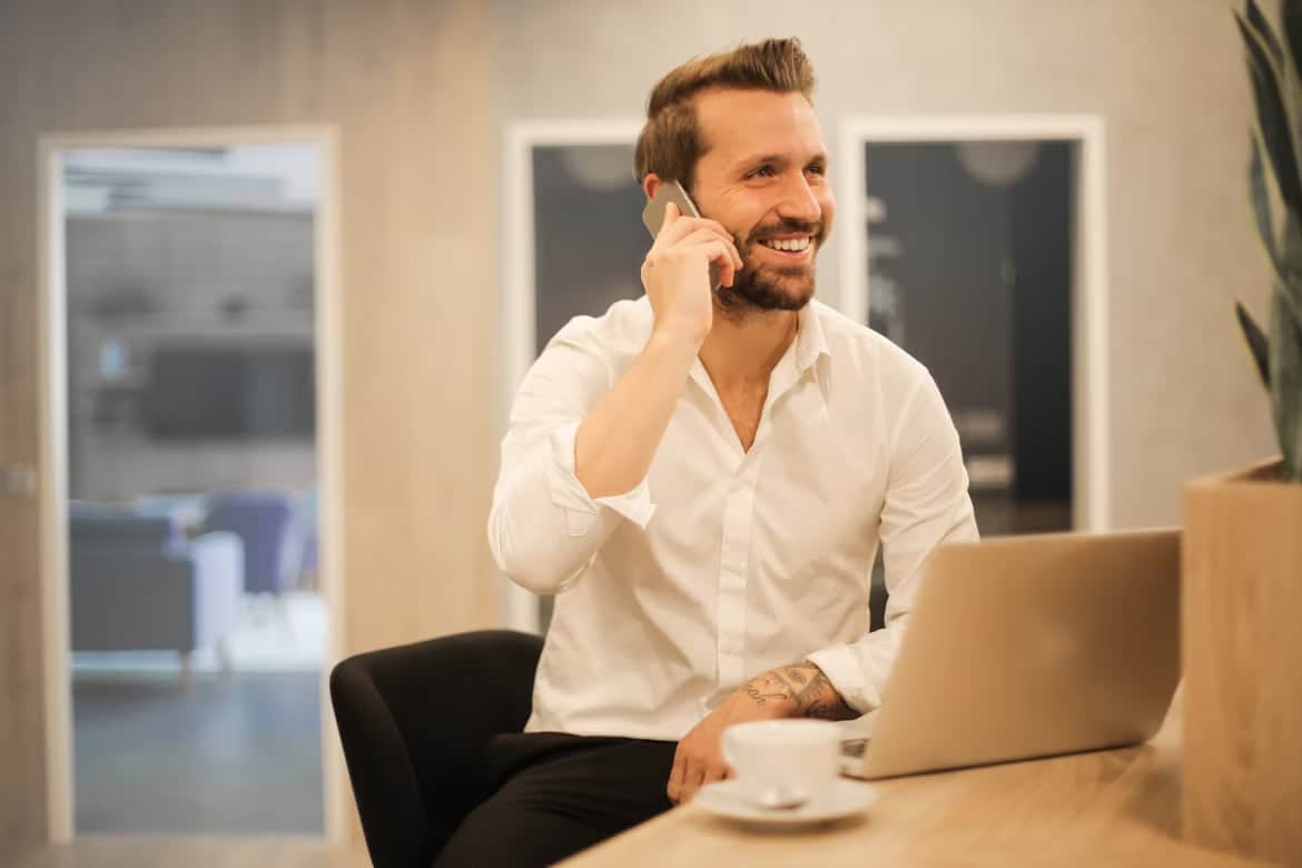 Besišypsantis vyras kalba telefonu prie kompiuterio
